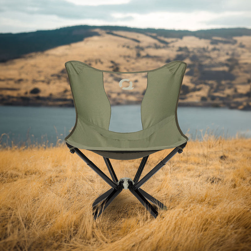 Burnt olive CLIQ MystiQ camping chair, with telescoping legs, in a field with a scenic background of hills and water.