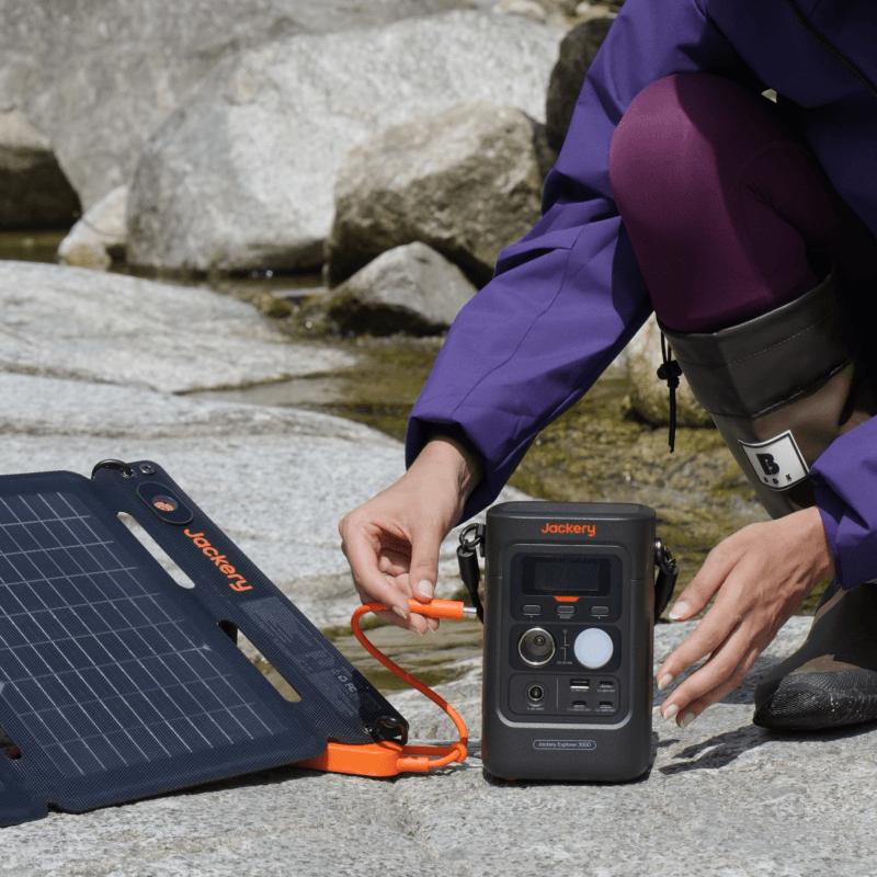 Person plugging a Jackery Explorer 300D compact portable power station and solar panel together outdoors.